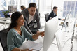 © fizkes - Boss and employee discussing work task at computer monitor in open office space. Female Latin professional showing online content, work report to male team leader at workplace
