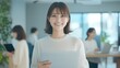 © Chotika88 - Smiling japanese business professional in modern office holding laptop bright environment positive atmosphere