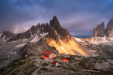 Wall Mural - aerial view of mountains, house and church at sunset in autumn. top view of high rocks, snow, purple