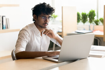 Remote work or learning. Focused young man in glasses student entrepreneur freelancer sit at office desk use notebook for design coding writing email surfing information online making project report