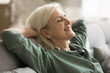 © fizkes - Emotional balance and inner peace. Carefree elderly woman pensioner recline on sofa in comfortable pose hands behind head dream with closed eyes breath fresh air relax at home alone. Close up portrait