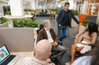 © Drobot Dean - A group of three employees sit and listen to a male employee standing next to them talking, in a meeting, during a retirement