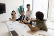 © fizkes - Group of four professionals engaged in collaborative discussion around conference table, reviewing documents, making charts data analysis, smiling, working on presentation. Teamwork and idea-sharing
