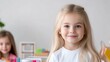 © Kaminashi Nozomi - A young girl with long blonde hair smiles at the camera. She wears a white shirt. Another child is blurred in the background. The image is well-lit, high-resolution, and has a soft focus. The style i