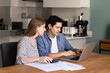 © fizkes - Focused young married couple managing family budget, check finances seated at table in modern kitchen, paying bills through secure e-banking system using laptop, make payment and virtual transactions