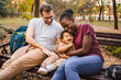 © Jelena - Mixed race couple is sitting on a park bench with their son