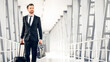 © Prostock-studio - Middle-aged handsome businessman walking by airport terminal with luggage and case, looking at copy space. Rich entrepreneur in black suit going by modern airport, departuring for business trip