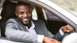 © Prostock-studio - Smiling african american entrepreneur in suit driving car, looking through window, panorama