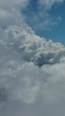 Wall Mural - flying through beautiful white fluffy clouds in blue sky. airplane travel background. vertical video