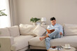 © New Africa - Man reading book on sofa in living room