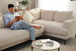 © New Africa - Man reading book on sofa in living room