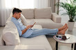 © New Africa - Man reading book on sofa in living room
