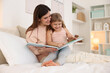 © New Africa - Bedtime. Happy little daughter reading book with her mother on bed at home