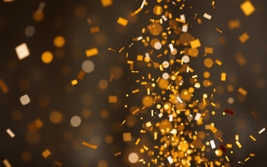 Wall Mural - golden confetti showers down against a blurred, dark backdrop, illuminated by warm golden bokeh ligh