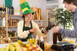 © JackF - Young woman seller offering bottle of whiskey to customer in grocery store decorated for St. Patrick's Day