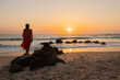 © Milou Dirks - silhouette of a woman in red dress standing on rocks in the ocean on the beach at sunset