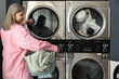 © zinkevych - Mature woman using self-service washing machine in laundromat