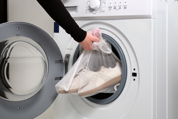 a women holds sports shoes in a laundry bag in a washing machine, open drum.