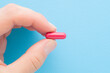 © fotoduets - Young adult woman hand fingers holding and showing red pill for improve of iron level in blood on light blue table background. Pastel color. Closeup. Top down view.