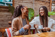 © carlesmiro - Two happy black women having coffee together in an outdoor cafe, laughing and enjoying. Mother and daughter.