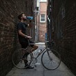 © sangram - A man is drinking water from a bottle while standing next to a bicycle
