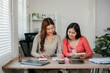 © Satori Studio - Two women working together at a home office desk, reviewing documents and taking notes in a bright, modern workspace.