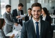 © Aklima - Portrait of smiling businessman with colleagues in background in a modern office setting indoors