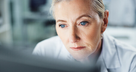 Thinking, scientist and woman with computer, lab and serious for research on web, reading and info. Healthcare, medical professional and mature person with tech for science, review and digital record