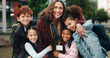 © BuyOutFelix01/peopleimages.com - Children, hug and smile with teacher, school and support in city for solidarity, connection or portrait. Happy kids, group and woman with embrace, education and outdoor for reunion with scholarship
