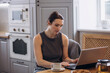 © kuzmichstudio - A beautiful brunette woman is in the kitchen at the table working on a laptop