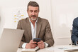 © Lomb - Senior businessman checking smartphone during office meeting
