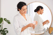 © Pixel-Shot - Beautiful young African-American woman applying micellar water on cotton pad near mirror in bathroom