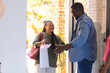 © Wavebreak Media - African American man welcoming woman with gift bag at home, both smiling warmly