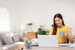 © Fahng - Smiling beautiful young woman, successful SME entrepreneur using laptop, typing on keyboard, working on freelance project online, holding coffee cup, working online