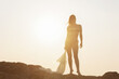 © Vladimir Razgulyaev - Silhouette of a woman in a swimsuit with a transparent cape in her hands standing on a rock against the sunset, close-up.