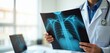 © miss irine - Doctor holds patient chest X-ray in medical office. Professional doctor wearing lab coat examines radiography. Healthcare tech for diagnosis, treatment, medicine. Modern clinic interior, stethoscope.