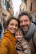 © Tobias - Close-up selfie of a happy family with a smiling toddler in a European city, enjoying their time together with love and affection.