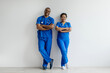 © Anastasiya - Portrait of two African American healthcare professionals in blue scrubs, confidently standing with arms crossed and smiling, posing together against a clean white studio background