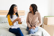 © Wavebreak Media - Young girl friends sitting on bed, sharing gift and smiling at home