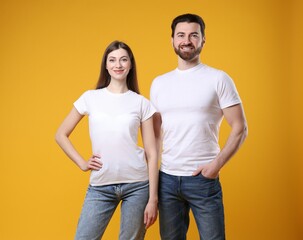 Wall Mural - woman and man wearing blank white t-shirts on orange background. mockup for design