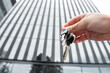 © RomanR - closeup Real estate agent holding key near house outdoors, high-rise buildings of modern city