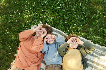Wall Mural - Top view of mother and two boys lying on picnic blanket together and making silly faces looking up copy space