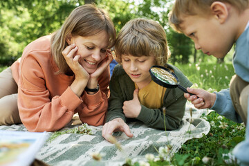 Wall Mural - Portrait of mother with two boys using magnifying glass in park and looking at bugs and insects exploring nature together