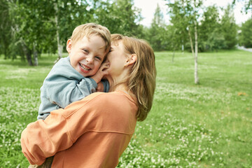 Wall Mural - Waist up portrait of mother holding little boy outdoors in sunlight and embracing playfully with son looking at camera copy space