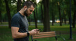 © Noor  - A focused young man checking his phone during a workout break in a serene park, wearing wireless earbuds, under soft evening light.