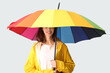 © Pixel-Shot - Young happy woman in raincoat with opened colorful umbrella on grey background