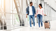 © Prostock-studio - Journey Together. Smiling Black Spouses Walking With Luggage In Airport Terminal, Romantic African American Couple Holding Hands While Going To Gate, Having Honeymoon Or Vacation Trip, Free Space