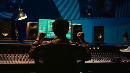 Leinwandbilder - African american sound engineer feeling happy with his recorded song on mixing console, working in music industry post production. Audio technician making a hit song in control room. Camera B.