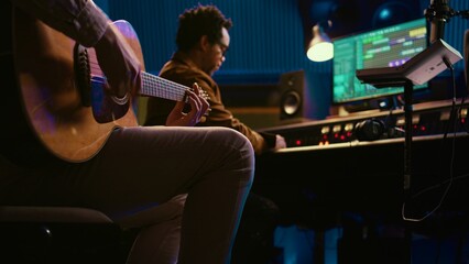 Leinwandbilder - Creative musician singing guitar in professional studio control room, recording his tracks with producer. Singer songwriter composing a new song for his album, editing tunes on console. Camera B.