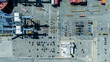 © Monet_P - Top-down aerial view of a busy port terminal showing rows of parked cars, shipping containers, cranes, and service vehicles. The image captures the scale and organisation of a logistics and transport